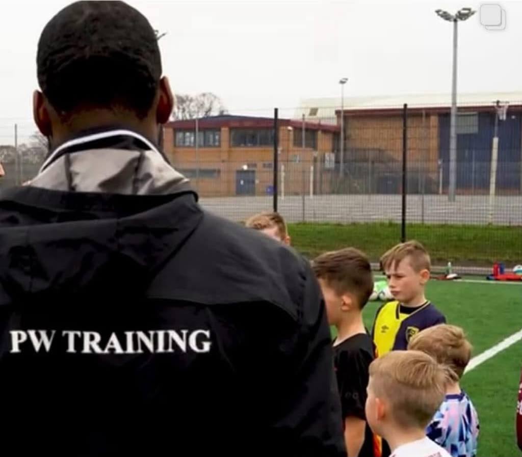 Coach Patrick in a PW Training jacket talking to a group of young players on the 3G pitch